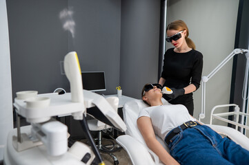 Young caucasian woman in goggles on photorejuvenation procedure. Doctor cosmetologist with a female patient.