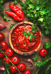 Caucasian cuisine. Traditional armenian hot adjika sauce with hot pepper, paprika, garlic and parsley on rustic wood kitchen table background, top view