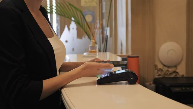 Female hands make payment for hotel reservation during work trip. Business woman using mobile phone for contactless payment on reception. Traveling woman paying smartphone on hotel lobby. Travel, job.
