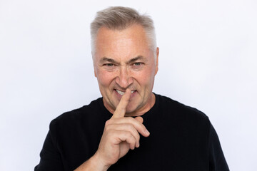 Portrait of angry senior man shushing. Displeased Caucasian male model in black T-shirt with gray hair looking at camera with finger on lips, asking to be quiet. Secret, silence concept.