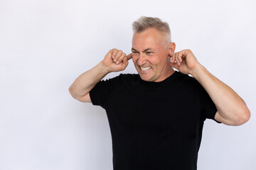 Senior man plugging ears with fingers. Male model in black T-shirt covering ears with serious angry face, frowning, shouting, gritting teeth. Portrait, studio shot, anger concept.