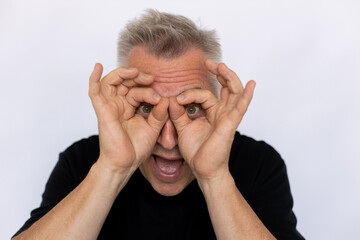 Senior man shaping glasses with fingers. Male model in black T-shirt making gesture forming goggles with both hands, having fun. Portrait, studio shot, making funny face concept.