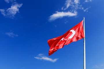 the flag of Turkey flutters against the blue sky with clouds. High quality photo