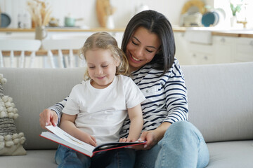 Obraz premium Mom, preschool daughter read book together, relaxing on cozy sofa, enjoying leisure together at home
