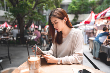 Business freelancer adult asian woman using digital tablet for work at sidewalk cafe