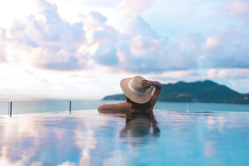 Rear view asia woman relax at outdoor luxury pool resort with sunset sky on holiday travel tropical
