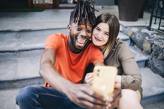 Multiethnic couple of best friends taking a selfie sitting on the stairs