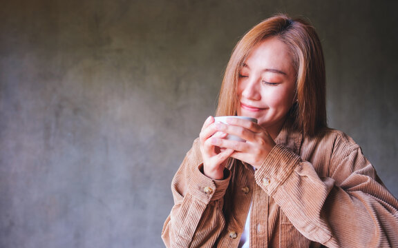 Portrait image of a beautiful young asian woman with closed eyes holding and drinking hot coffee in cafe