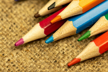 Several colored pencils of different colors on a background of coarse burlap. Close-up, selective focus.