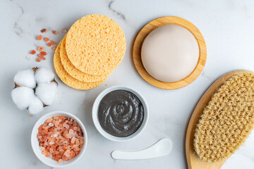 Top view of spa cosmetics products. Clay mask, massage brush with natural bristle, cosmetic sponges, natural soap and himalayan sal to marble table