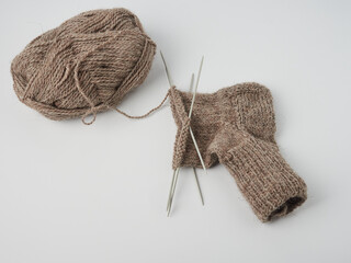 Knitting socks. Needlework in progress. Top view photo of brown sock made of natural wool, needles...