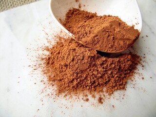 cocoa powder in a spoon on a light marble background