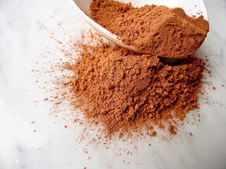 cocoa powder in a spoon on a light marble background