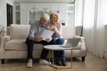 Attractive older couple reading received formal notification, smiling enjoy news, feel satisfied look happy, get mortgage approval, relish financial success, investment and profits, pension growth
