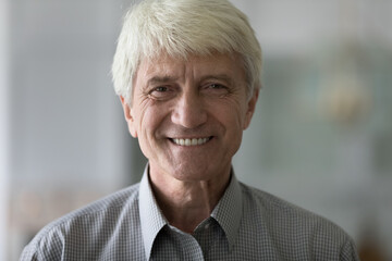 Close up handsome face of elderly man having candid wide toothy smile standing indoors look at...