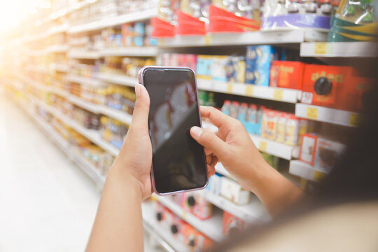 woman hand using smart phone over blurred image of supermarket, shopping online on mobile