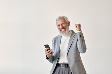 Excited overjoyed happy old senior business man investor winner raising fist holding cell using smartphone winning mobile bet money prize holding cellular phone celebrating victory isolated on white. - Powered by Adobe