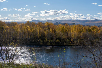 Autumn city landscape, view from the mountain to the river, and the bridge. Yellowing beautiful forest in the city park.