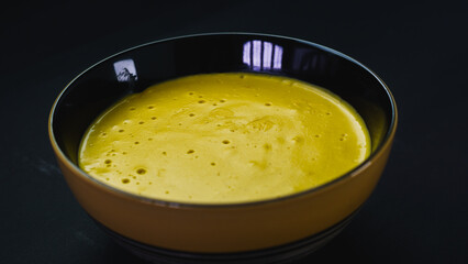 yellow and black ceramic bowl filled with pumpkin puree on a black background. Foodie.