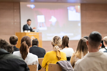 Speaker giving a talk in conference hall at business event. Rear view of unrecognizable people in audience at the conference hall. Business and entrepreneurship concept.