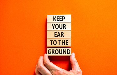 Keep your ear to the ground symbol. Concept words Keep your ear on the ground on wooden blocks. Businessman hand. Beautiful orange background. Business keep your ear on the ground concept. Copy space.