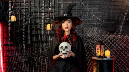 Beautiful woman wearing witch costume holding skull in halloween theme