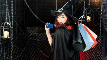 Beautiful young woman in witch costume show credit card holding shopping bags in halloween theme.
