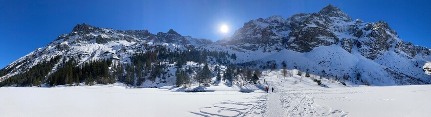 Winter mountains with snow in the winter rocky landscape. Winter nature landscape with mountains, trees, forest, plants and blue sky with clouds and sun. Hiking in the mountain with snowy path. 