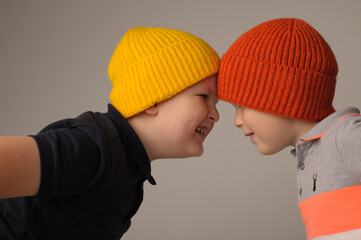 studio photo of two brothers aged 5 and 7 in bright knitted autumn hats on a gray background