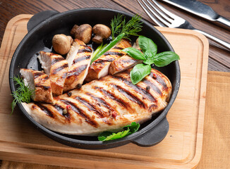 Roasted chicken fillet and mushrooms with herb in the frying pan on the wooden table close-up.