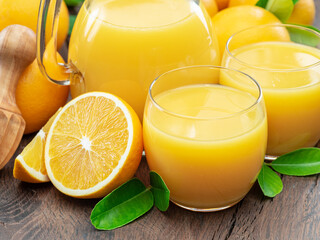 Glasses of fresh orange juice and orange fuits near them isolated on dark wooden background. Close...