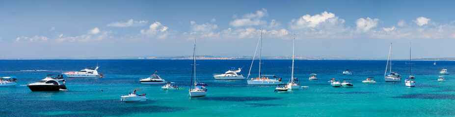 Fototapeta na wymiar Panorama of a azure bay near Alicante resort with sea sailing yachts and boats, Spain. Wide panorama with coastline of Tabarca Island with many sailing ships and tourist at sea.