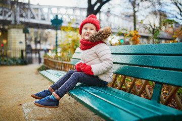 Happy preschooler girl sitting on the bench on a street of Paris, France