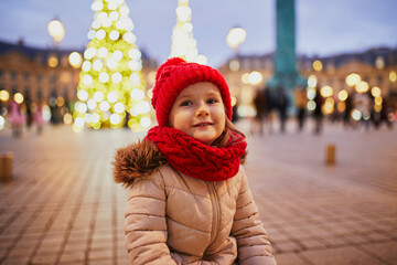 cheerful preschooler girl in red hat on Place Vendome decorated for Christmas in Paris, France