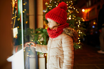 Obraz premium Preschooler girl looking at window glass of large department store decorated for Christmas