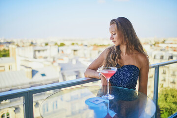 Fototapeta na wymiar Young woman drinking alcoholic cocktail in a rooftop restaurant with view to the Eiffel tower in Paris, France