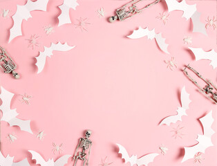 Halloween frame of white paper bats, skeletons and spiders on pastel pink background.