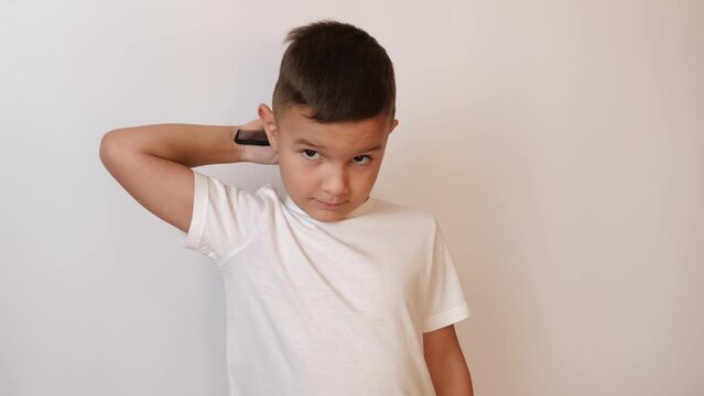 A cute little boy is trying to comb his hair with a comb.