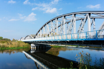 Naklejka premium Metal bridge background. Road bridge construction. Empty asphalt road. Blue sky weather long bridge over Narew river. Tykocin village in Poland.