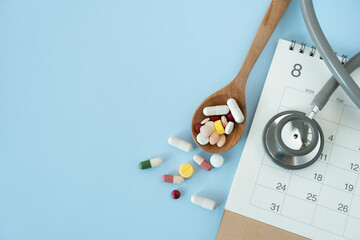 Plan to eat pills or drugs on time, with stethoscope, calendar on blue table background, healthy and medicine concept