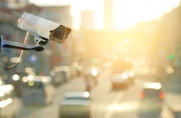 Double exposure of modern public CCTV camera on traffic roads at sunset background with copy space.