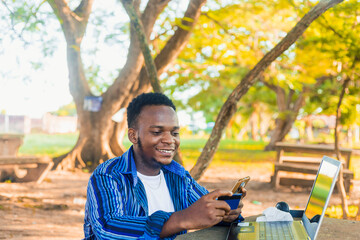 young cheerful african male student shopping online with mobile phone and bank card in hand