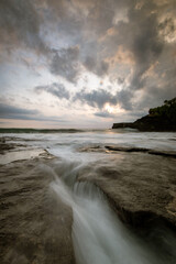 Sunset in tanah lot, bali with big rock cliff and coral reef using long exposure