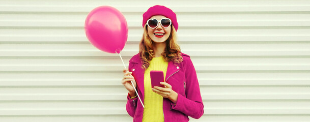 Portrait of happy smiling young woman with phone and pink balloons wearing beret on white background