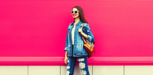 Fototapeta na wymiar Portrait of happy smiling young woman looking away wearing denim jacket with backpack on colorful pink background, blank copy space for advertising text