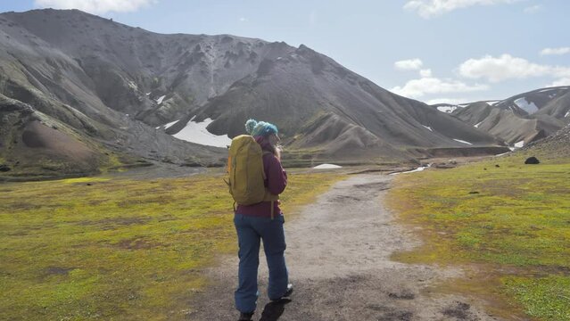 travel experience solo hiker female walking into wilderness mountain landscape,woman explorer discover untoched wild nature,traveler girl walks in the valley of landmannalaugar enjoying the view