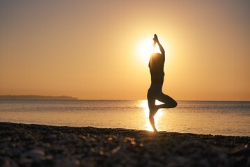 Silhouette young woman practicing yoga on the beach at amazing sunset. High quality photo