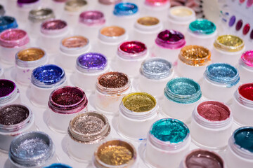 Colorful makeup glitters in plastic cosmetic jars in row on counter for sale in cosmetics shop, tradeshow. Glamour, fashion, make up, beauty and skincare concept