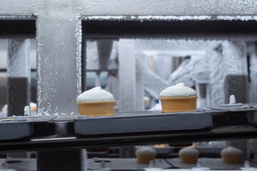 Conveyor belt with ice cream cones - icecream automatic production line on dairy factory: close up. Manufacturing, dairy industry, food processing, and automated technology equipment concept