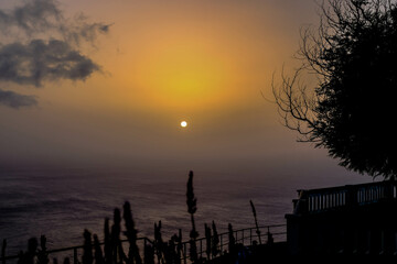 The sun sets in the sea on a hazy sunset from the Fio viewpoint west of Mdeira